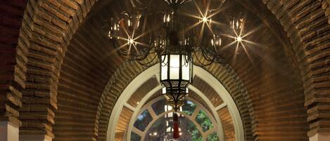 An arched hallway with a chandelier, a fountain, and a view into a garden.
