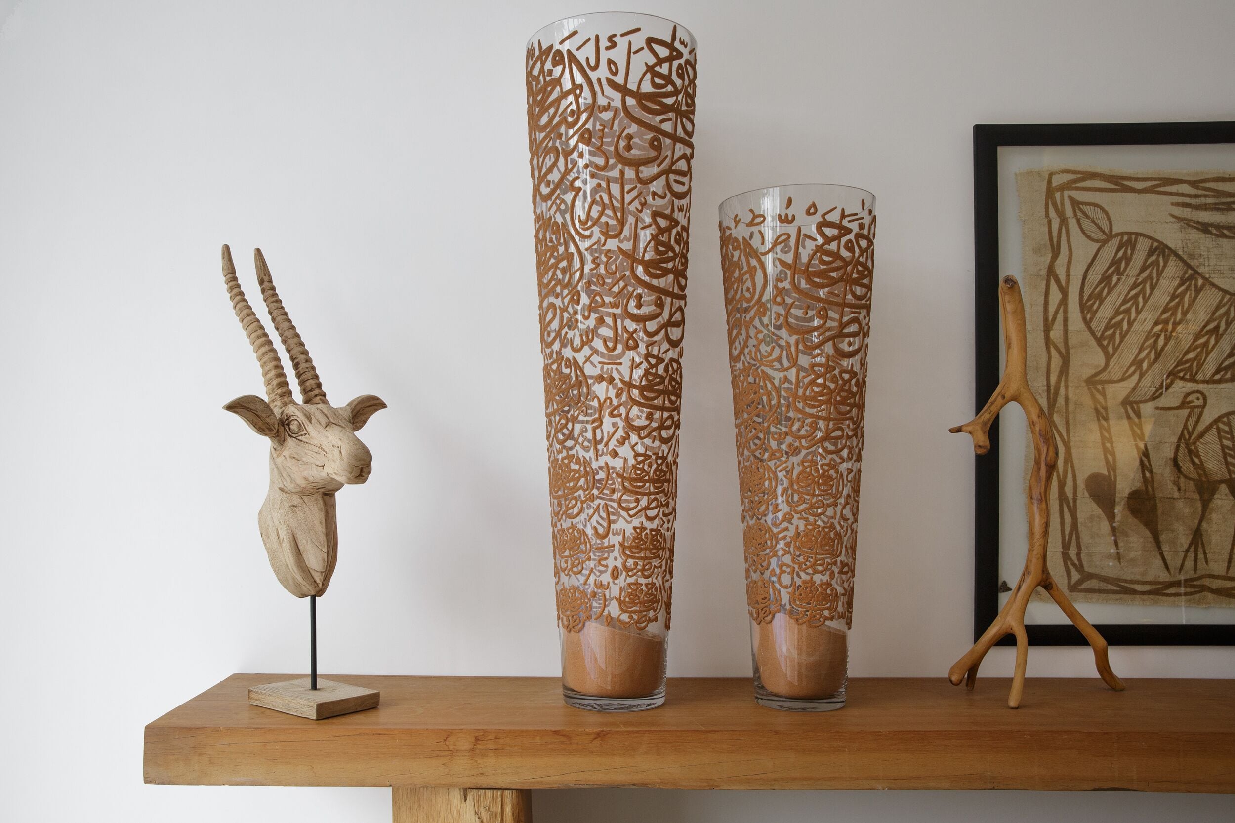Three tall, intricately designed vases on a wooden shelf, a wooden sculpture, and a framed artwork.