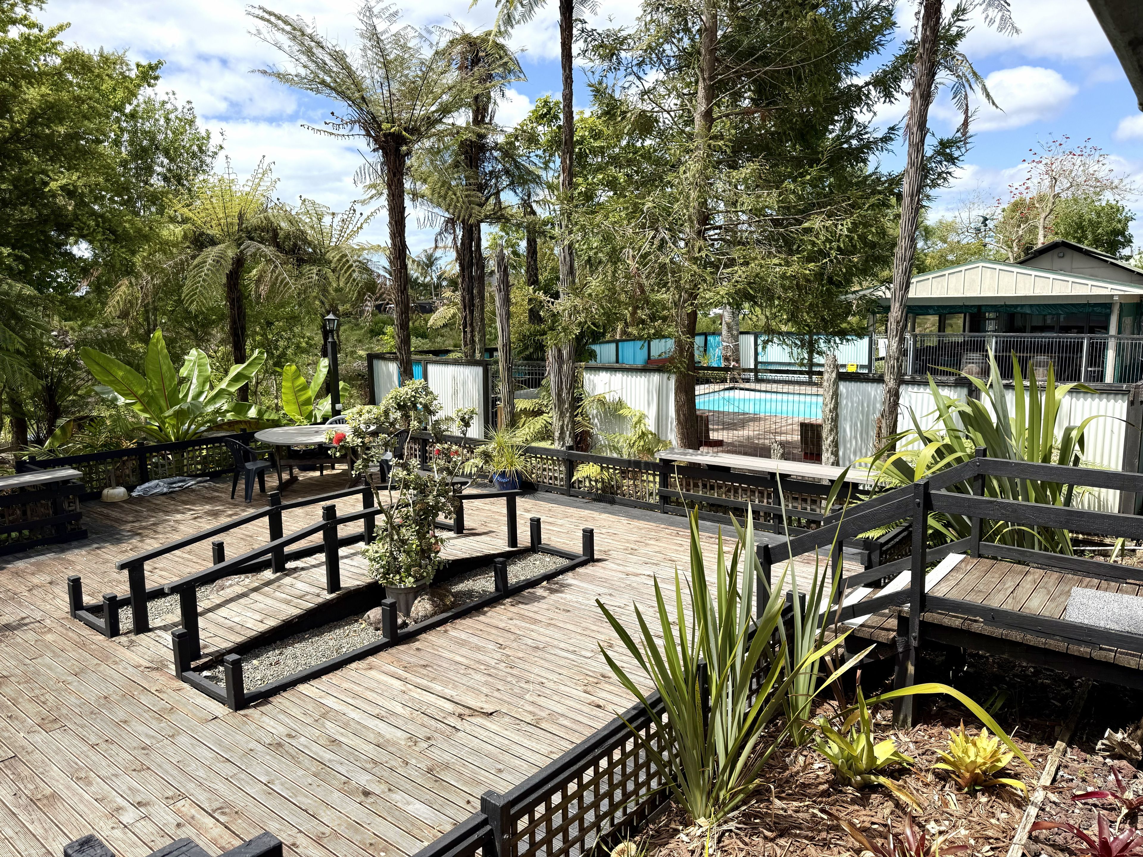 A wooden deck with outdoor seating, surrounded by lush greenery and a pool area.