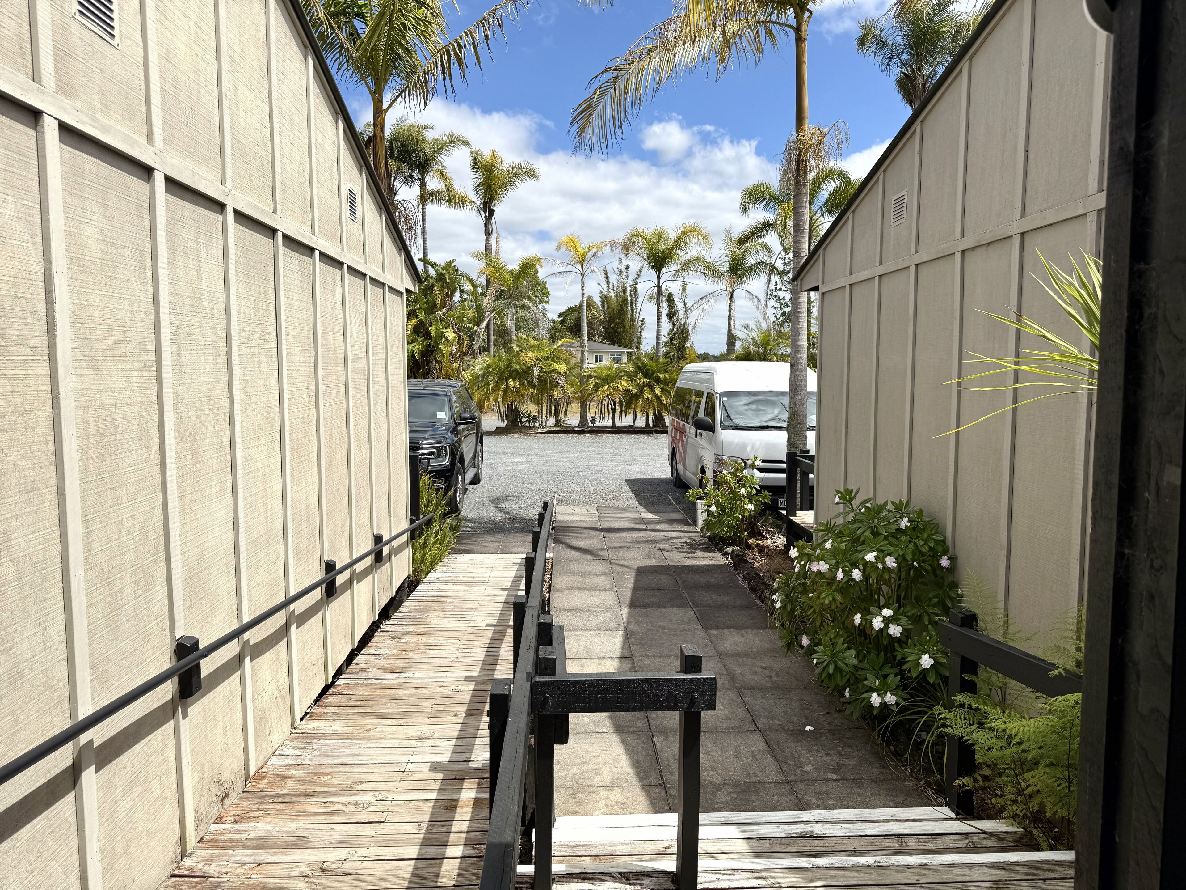 A narrow pathway flanked by buildings with parked vehicles, leading to a gated entrance.