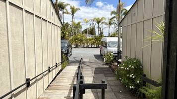 A narrow pathway flanked by buildings with parked vehicles, leading to a gated entrance.
