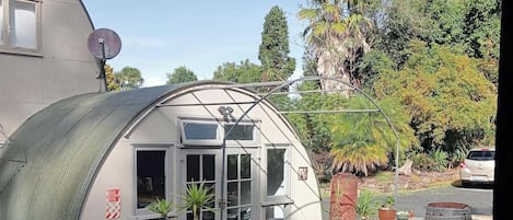A greenhouse with a curved roof, wooden deck, and potted plants.