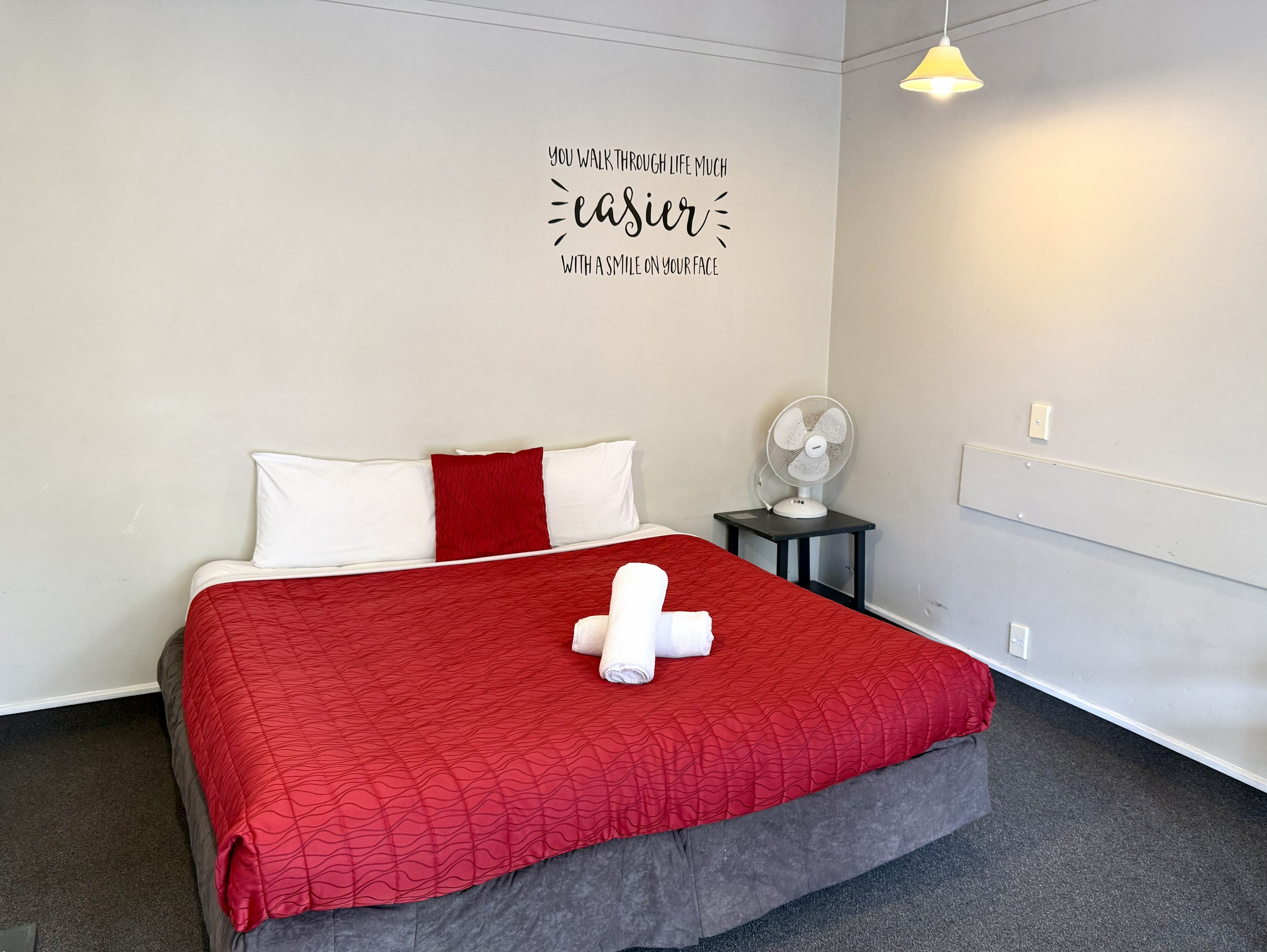 Una habitación de hotel con cama, ventilador de pared y una frase motivacional.