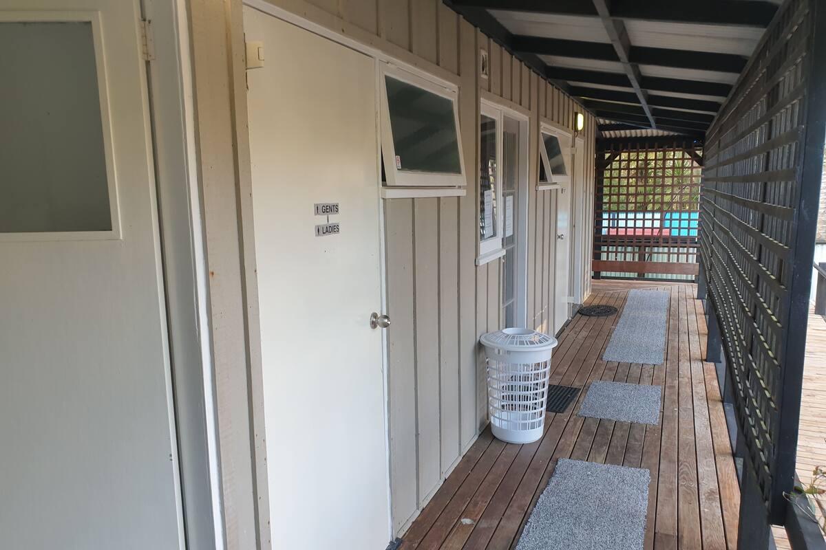 A corridor with doors marked for 'Gents' and 'Ladies', a white basket, and a wooden deck with mats.