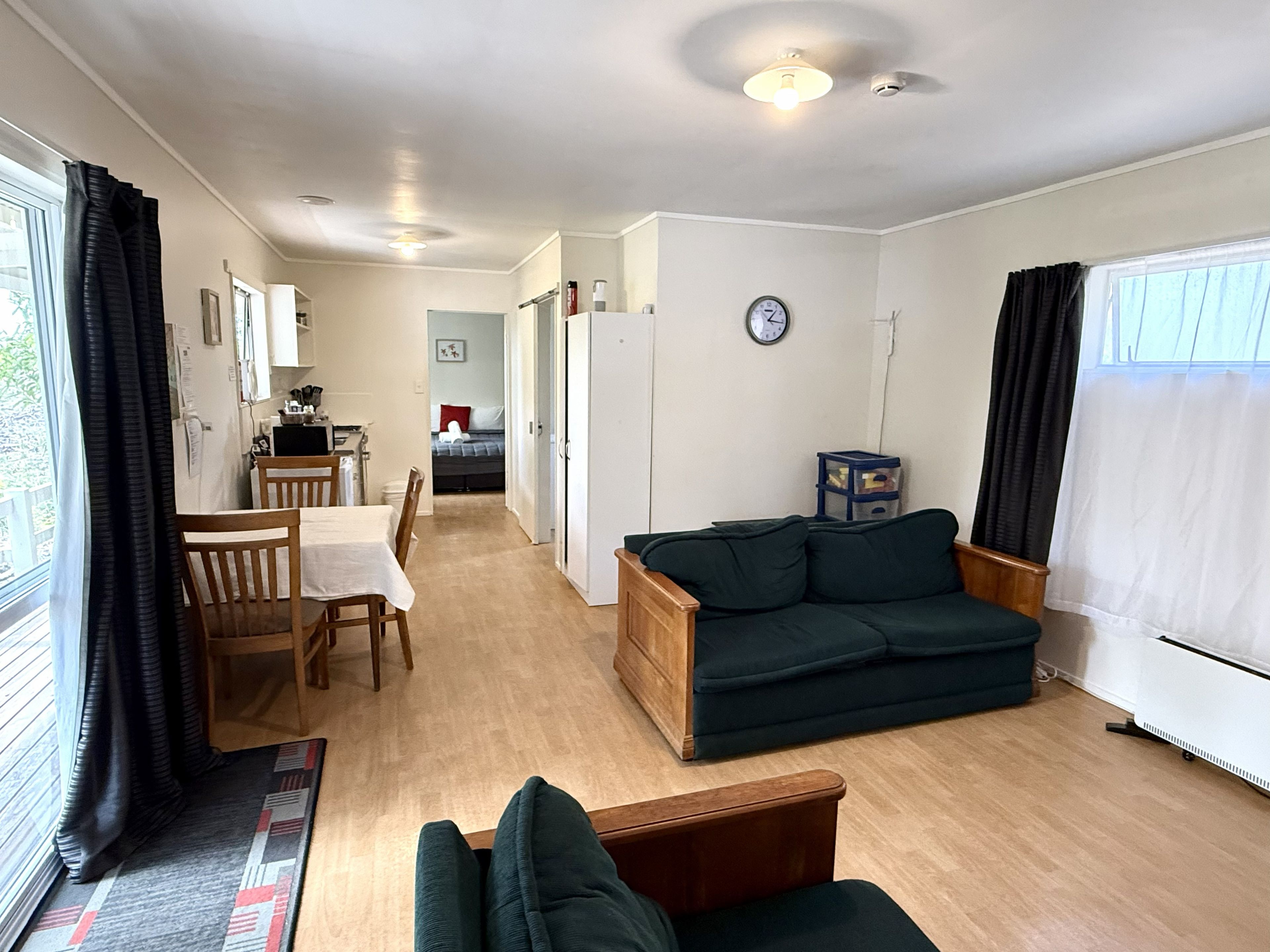 A compact living space with a dining area, a sofa, a small kitchen, and a view through a window.