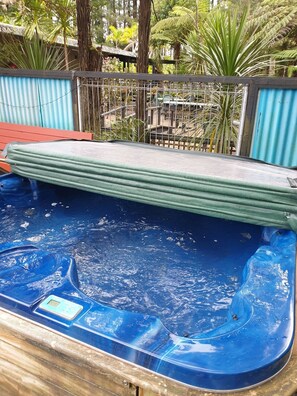 A hot tub with a digital thermometer, surrounded by a metal fence and various plants.