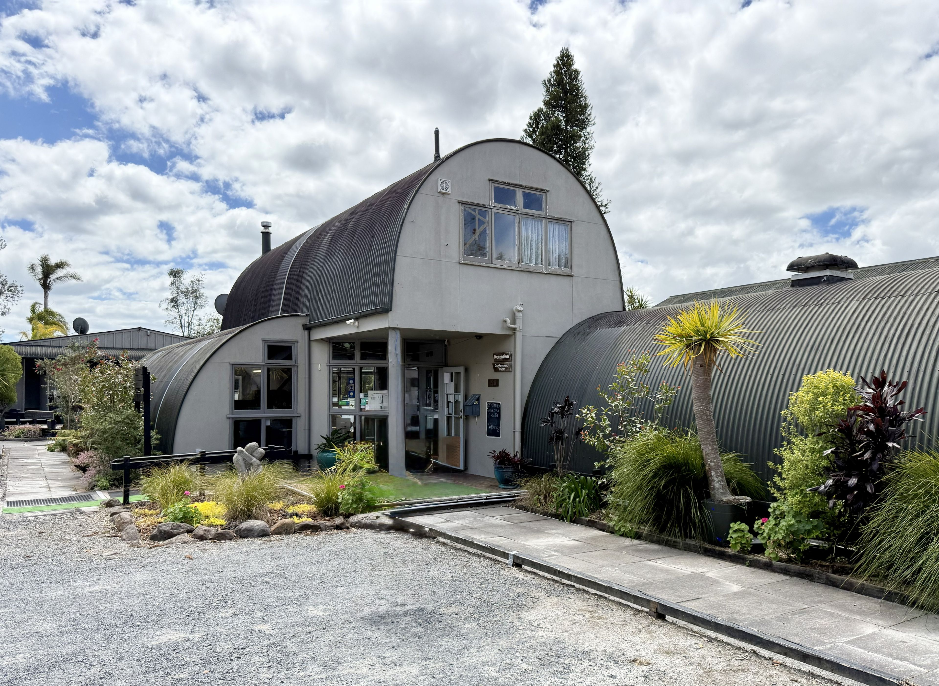 A modern building with a curved roof, large windows, and a sign indicating a reception area.