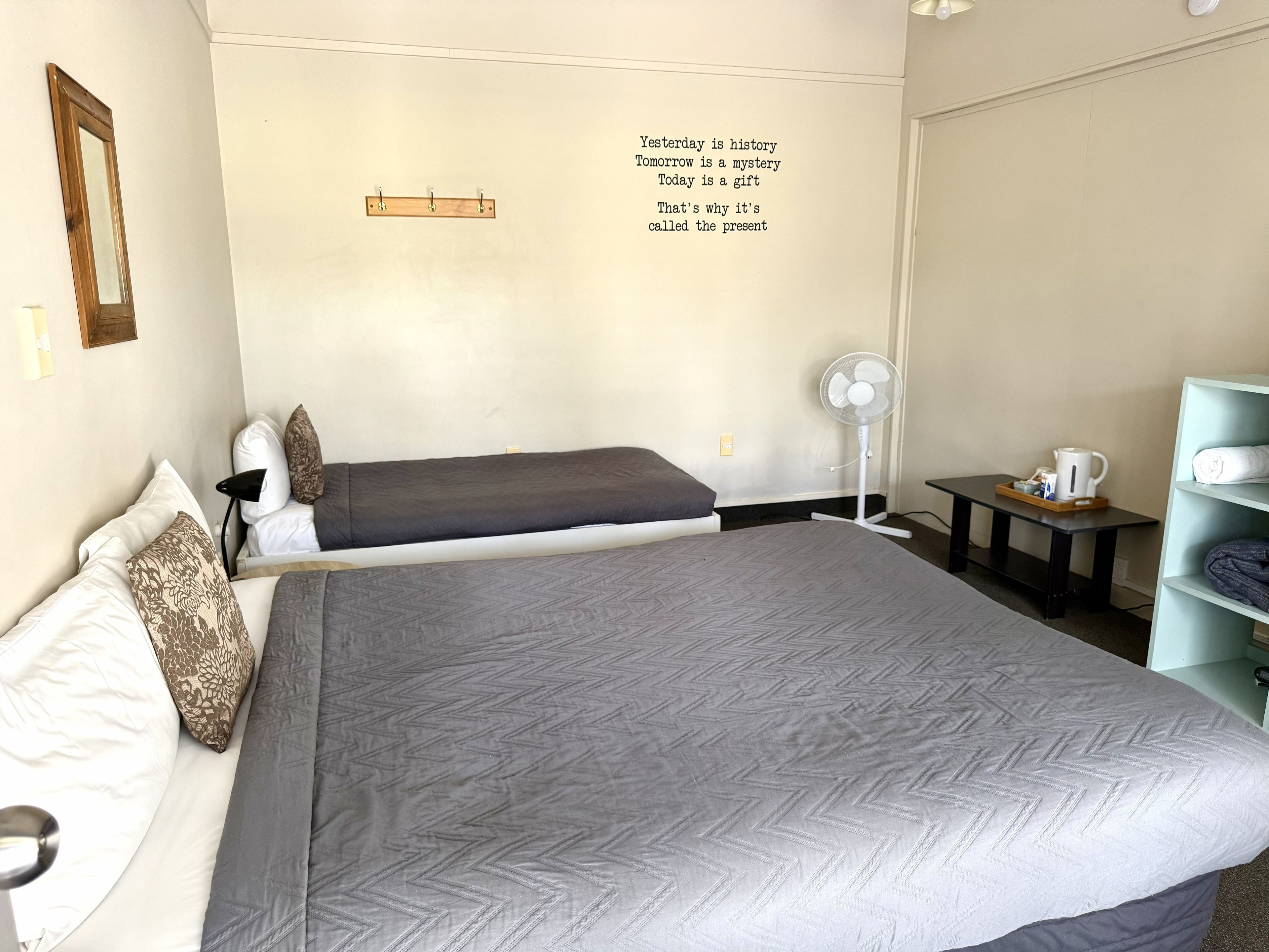 Ein Schlafzimmer mit einem großen Bett, einem Nachttisch mit Ventilator, einem Regal mit Handtüchern und einer Wand mit motivierenden Texten.