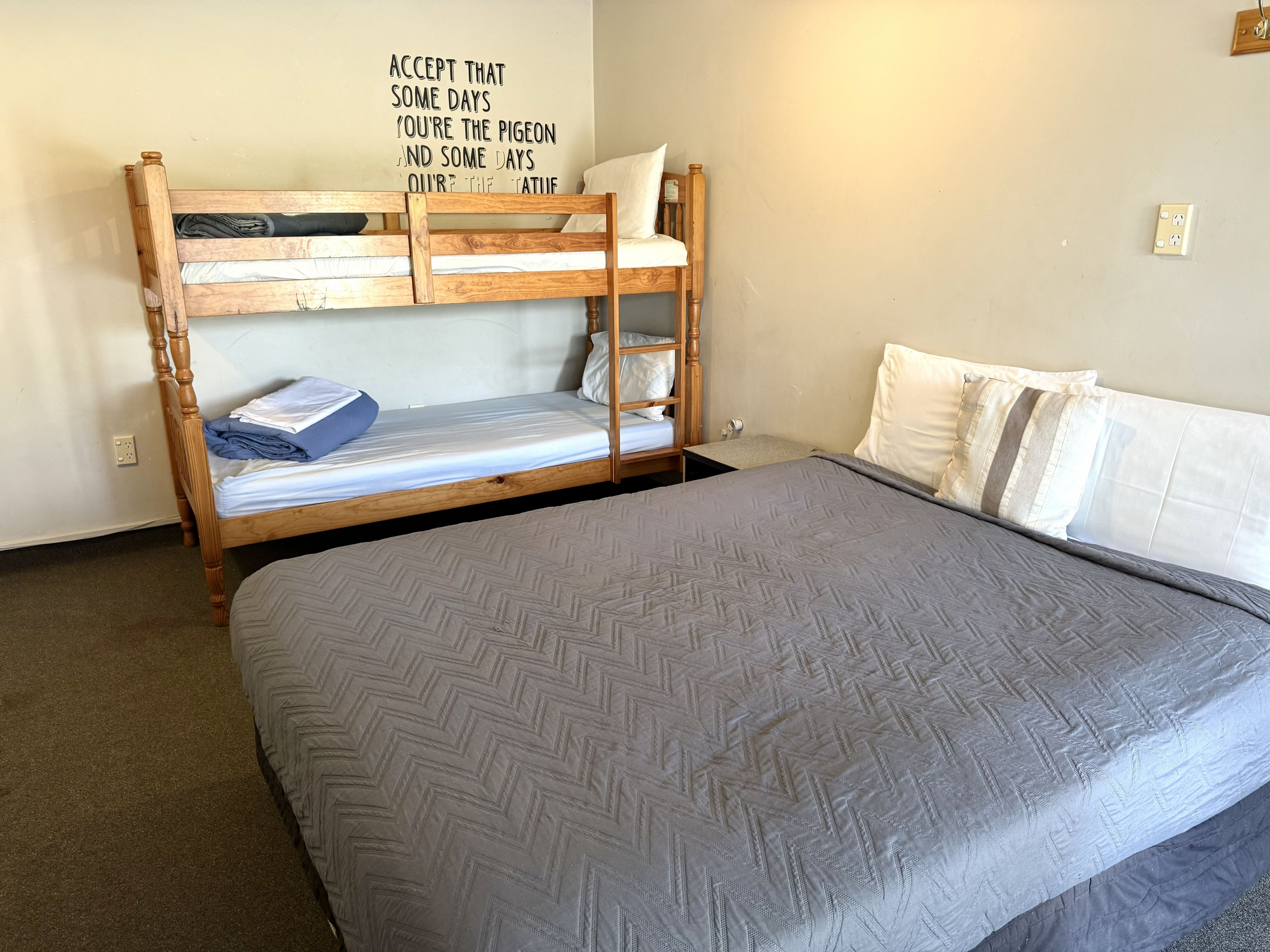 A bunk bed with a motivational quote on the wall, a single bed with a grey quilt, and a power outlet on the wall.