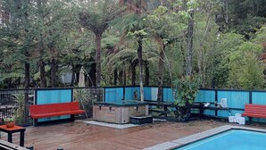 Uma piscina com deck de madeira, bancos vermelhos e uma banheira de hidromassagem.