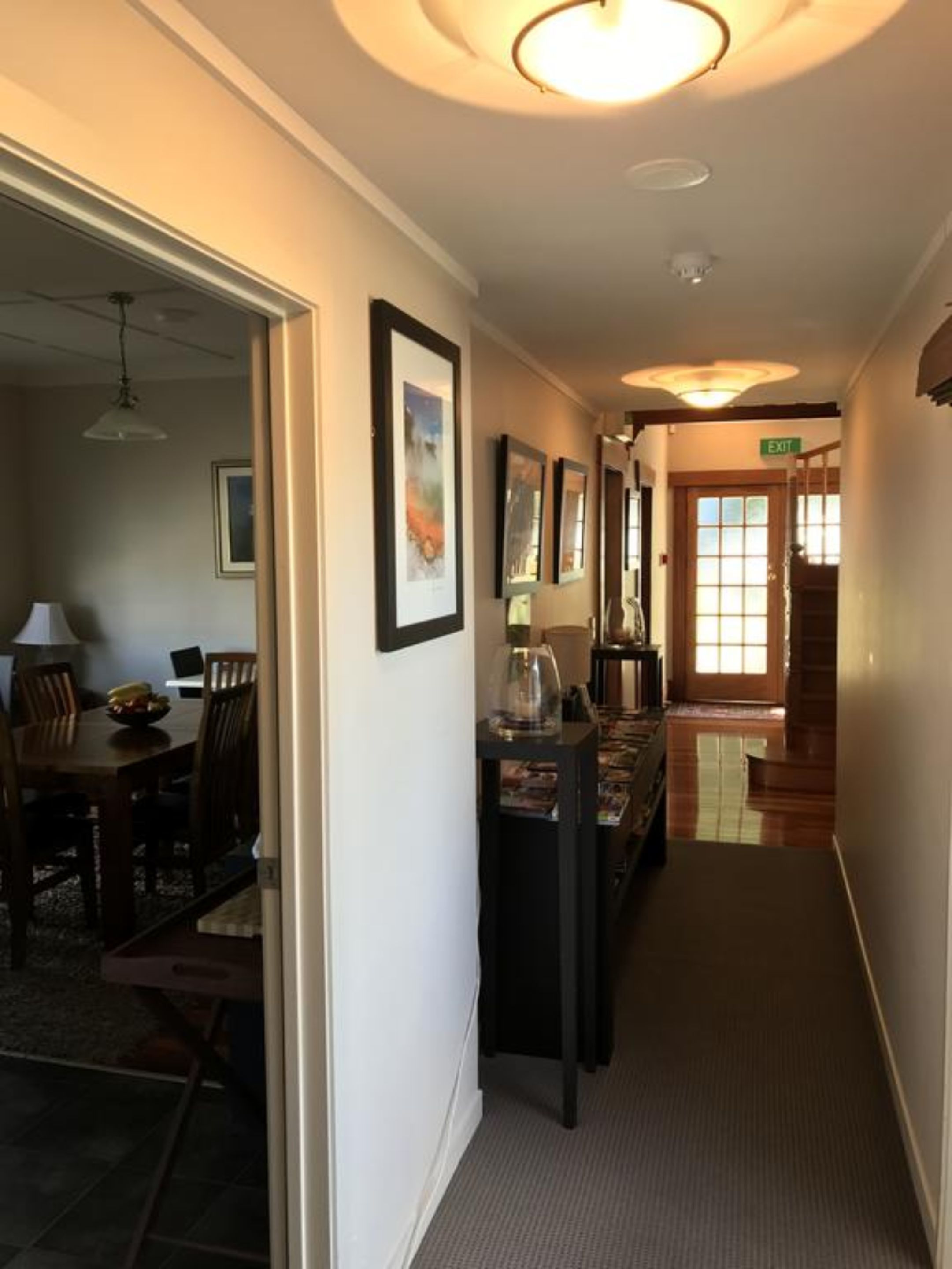 A hallway with framed artwork on the walls, a dining area with a table and chairs, and an exit sign.
