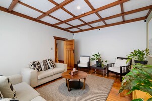 A spacious living room with a high ceiling, wooden beams, a sofa, two armchairs, a coffee table, and potted plants.