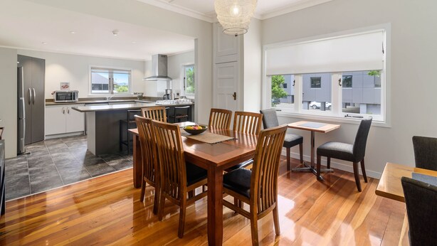 A modern kitchen with a central island, wooden dining table with chairs, and a large window with a view of the street. - Lake Lodge B&B Rotorua - Adults Only (Rotorua)