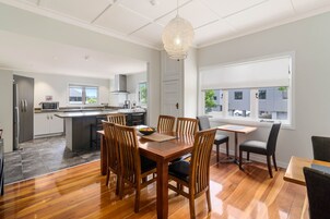 A modern kitchen with a central island, wooden dining table with chairs, and a large window with a view of the street.
