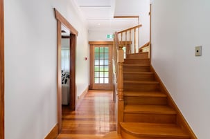 A wooden staircase leading to a second floor, a door with frosted glass panels, and a hallway with a patterned rug.