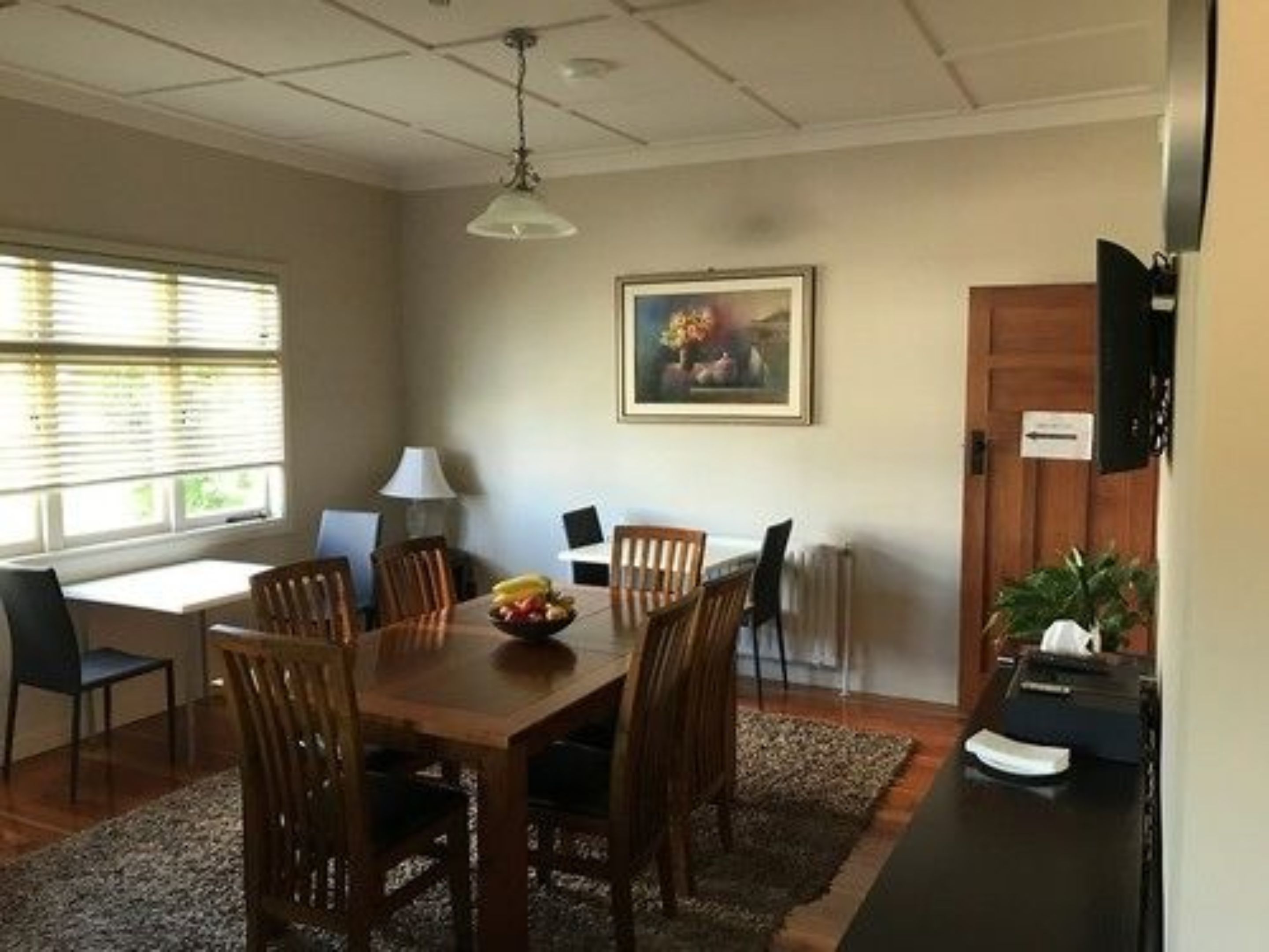 Un coin repas avec une table en bois, des chaises, un panier de fruits, une lampe et un tableau accroché au mur.