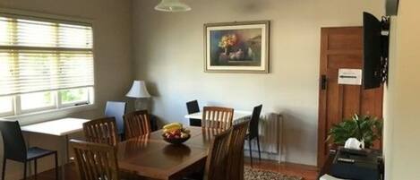 Un coin repas avec une table en bois, des chaises, un panier de fruits, une lampe et un tableau accroché au mur.