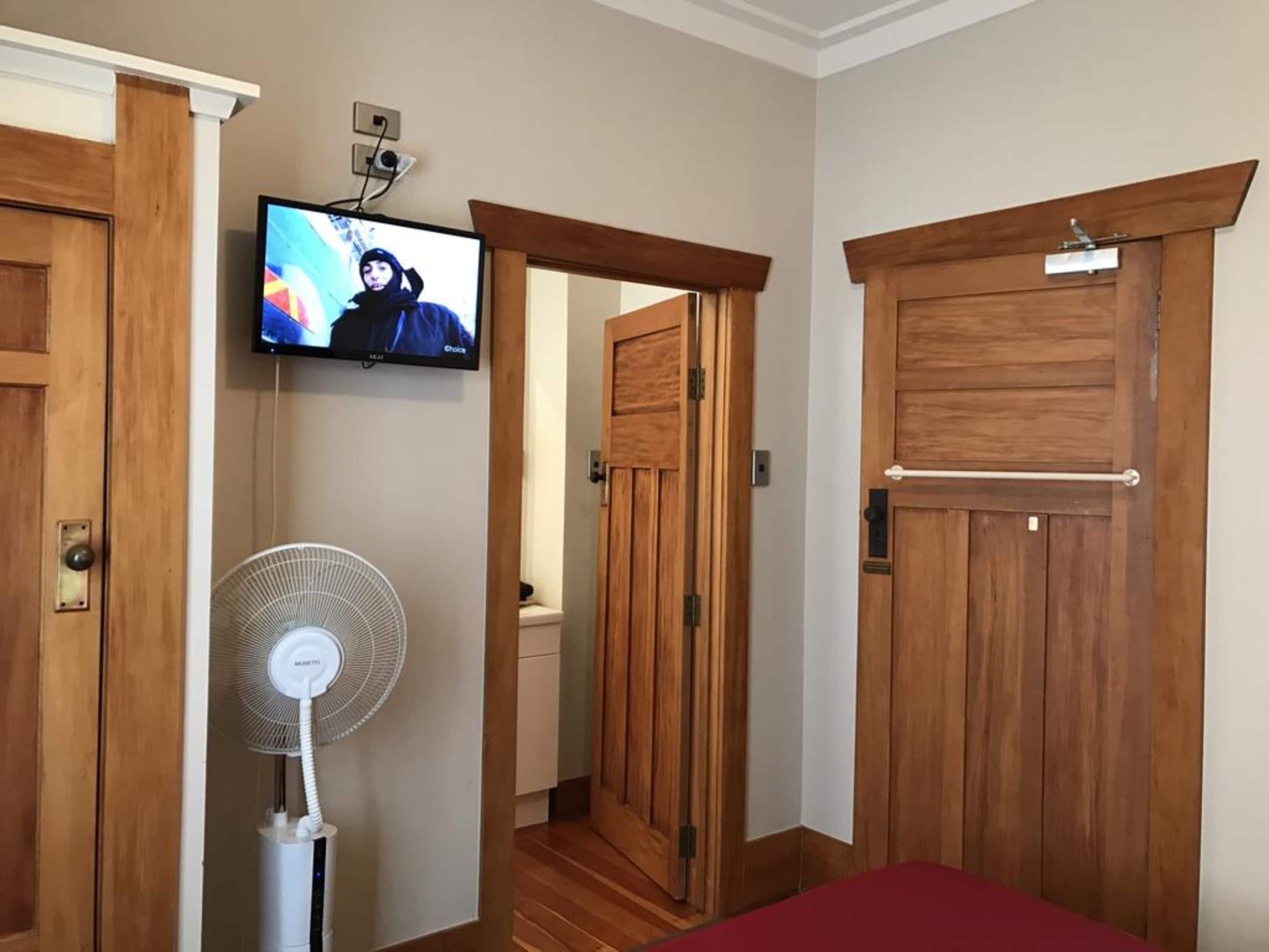 A room with wooden doors, a mounted television, and a standing fan.