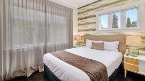 A hotel room with a large bed, a nightstand, a lamp, and a window with a view of trees. - Lake Lodge B&B Rotorua - Adults Only (Rotorua)