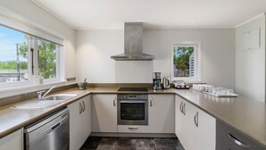 A modern kitchen with a stainless steel dishwasher, oven, and sink. There is a large window providing a view of the outdoors. - Lake Lodge B&B Rotorua - Adults Only (Rotorua)