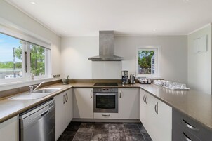 A modern kitchen with a stainless steel dishwasher, oven, and sink. There is a large window providing a view of the outdoors.