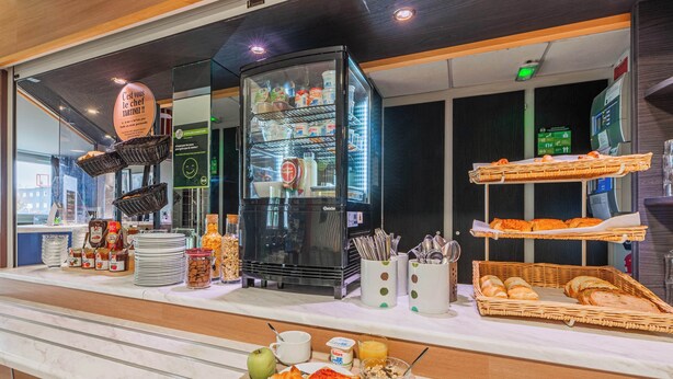 Un bufé de desayuno con diversas opciones de comida, un refrigerador y panes en cestas.