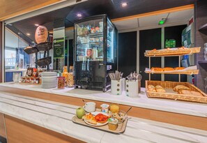 A breakfast buffet with various food items, a refrigerator, and baskets of bread. - B&B HOTEL Mulhouse Kingersheim (Kingersheim)