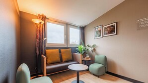 Una habitación moderna con un sofá, dos sillones, una mesita, una lámpara, un ventanal y una planta.