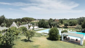 Un área de piscina con sillones de descanso, un porche cubierto y vistas del paisaje circundante.