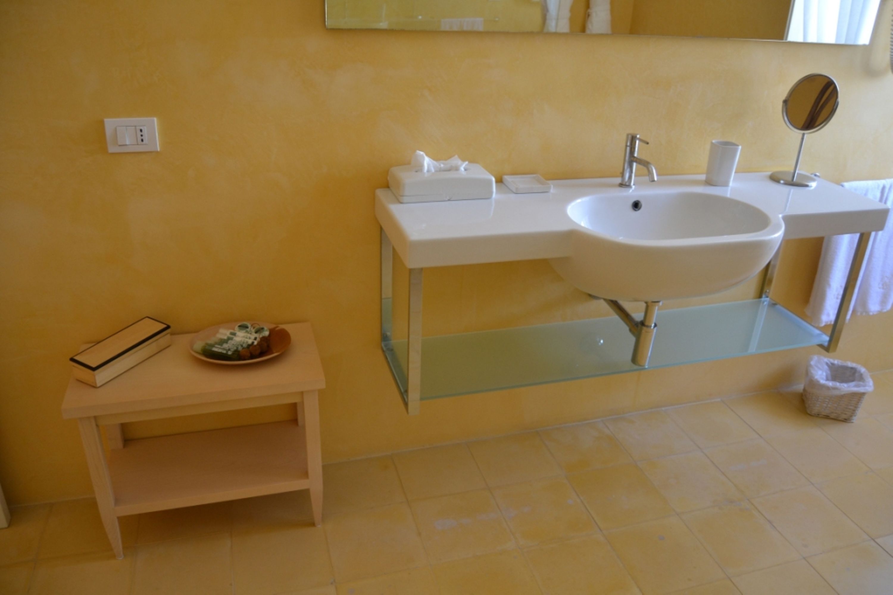 A bathroom with a white sink, a mirror, a towel rack, and a small shelf with a book and a plate.