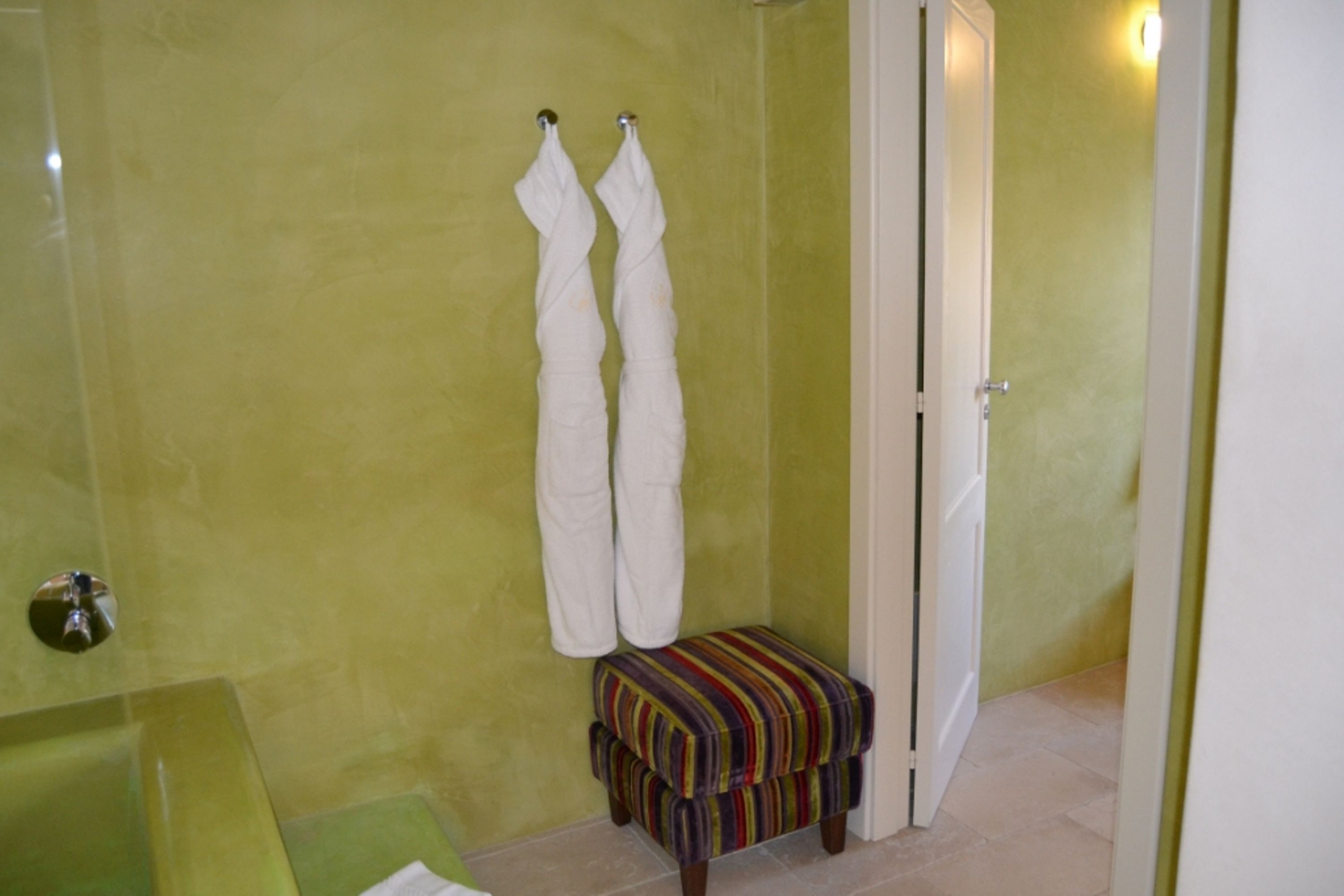 Un baño con pared verde, bañera blanca y banca a rayas.