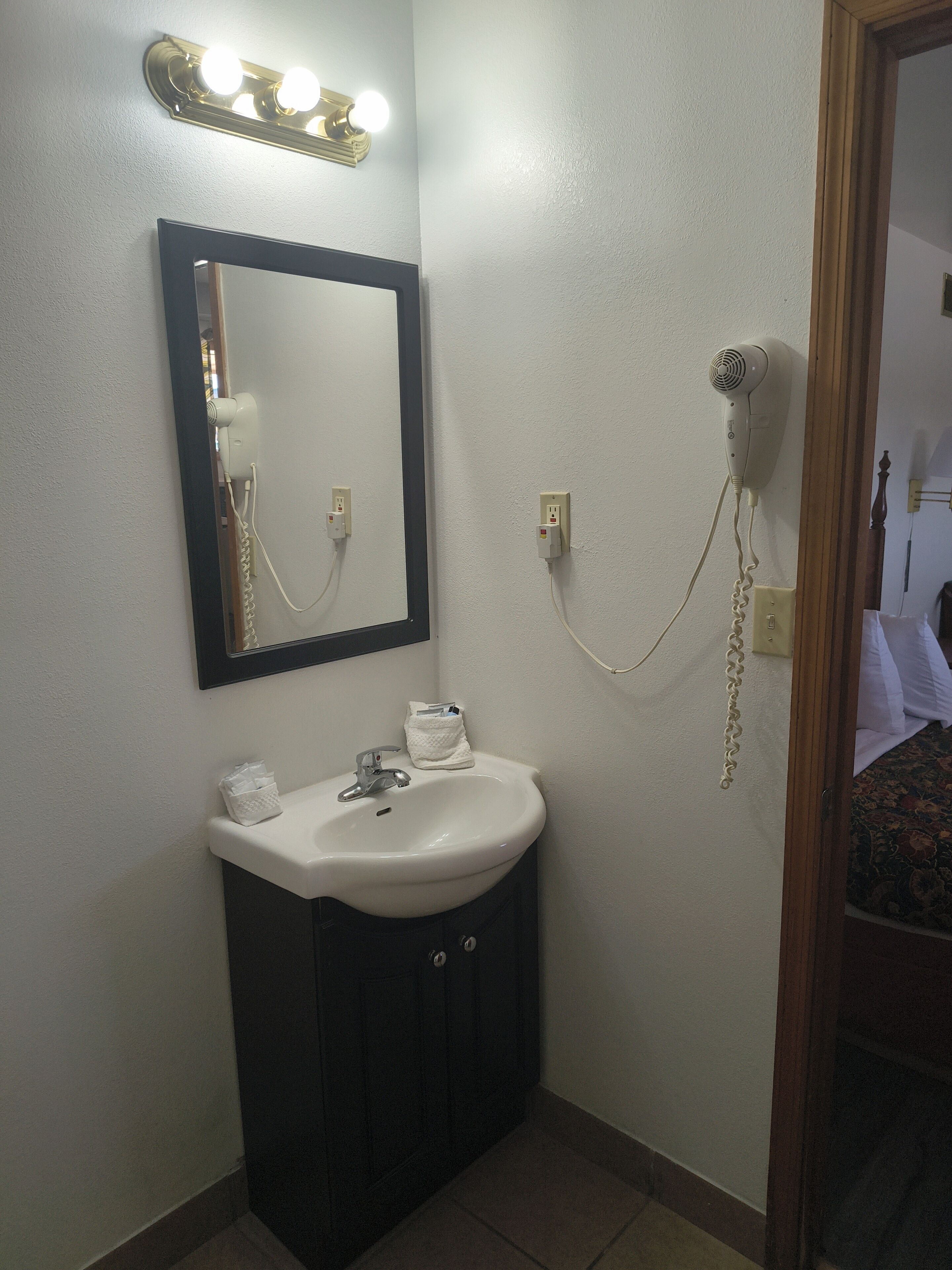 A bathroom with a sink, mirror, hairdryer, and lights.