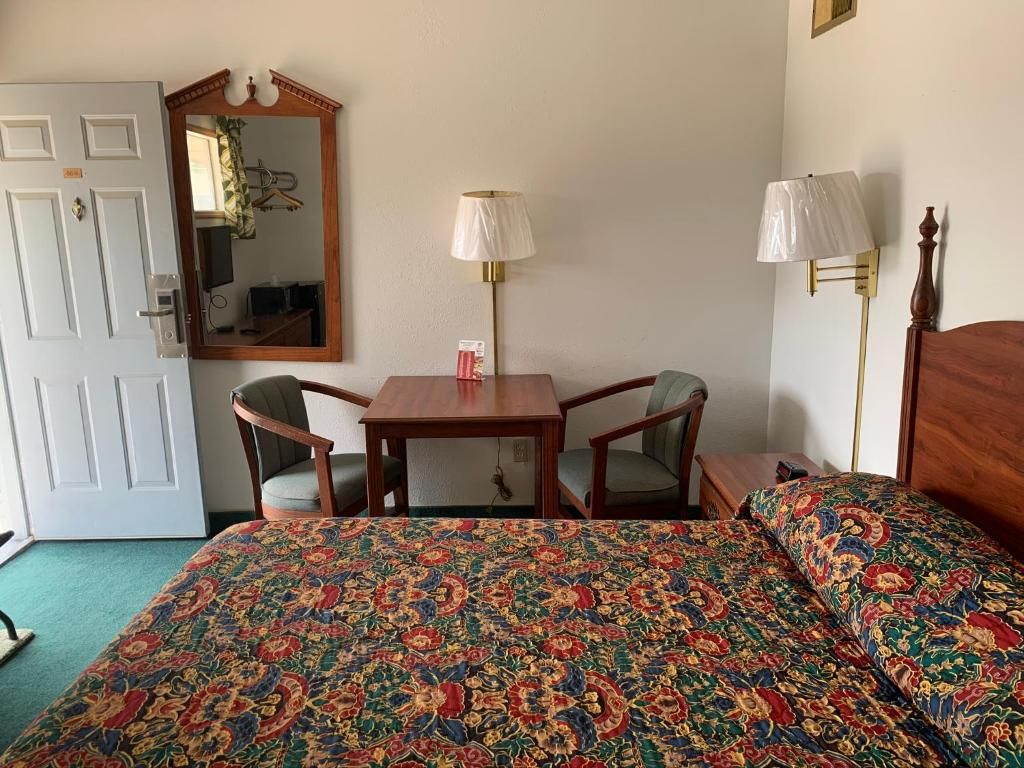 Una habitación de hotel con una cama, dos sillas, una mesa, un espejo y dos lámparas.