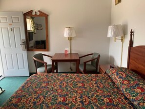 A hotel room with a bed, two chairs, a table, a mirror, and two lamps. - Budget Lodge Inn Abilene KS (Abilene)
