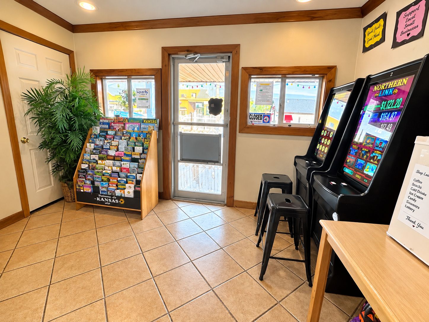 A room with a door, a display of postcards, a vending machine, and a sign with a list of items.