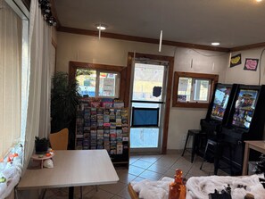 A room with a table, a plant, a bulletin board with travel brochures, and two slot machines. - Budget Lodge Inn Abilene (Abilene)