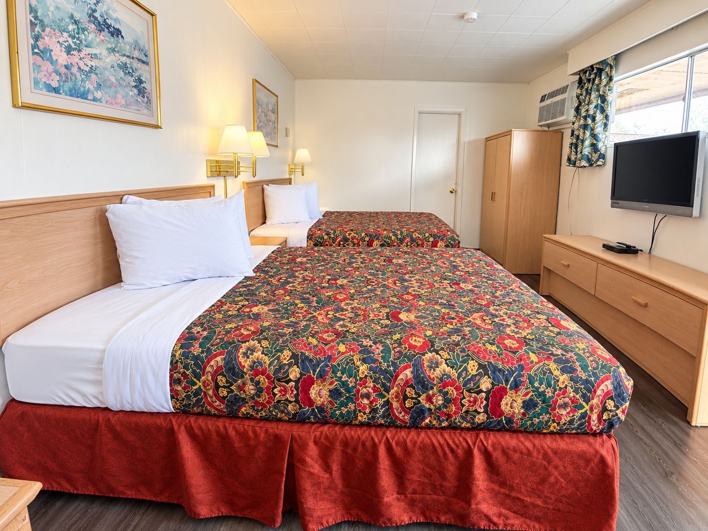 A hotel room with two beds, a TV, a wardrobe, and a painting on the wall.