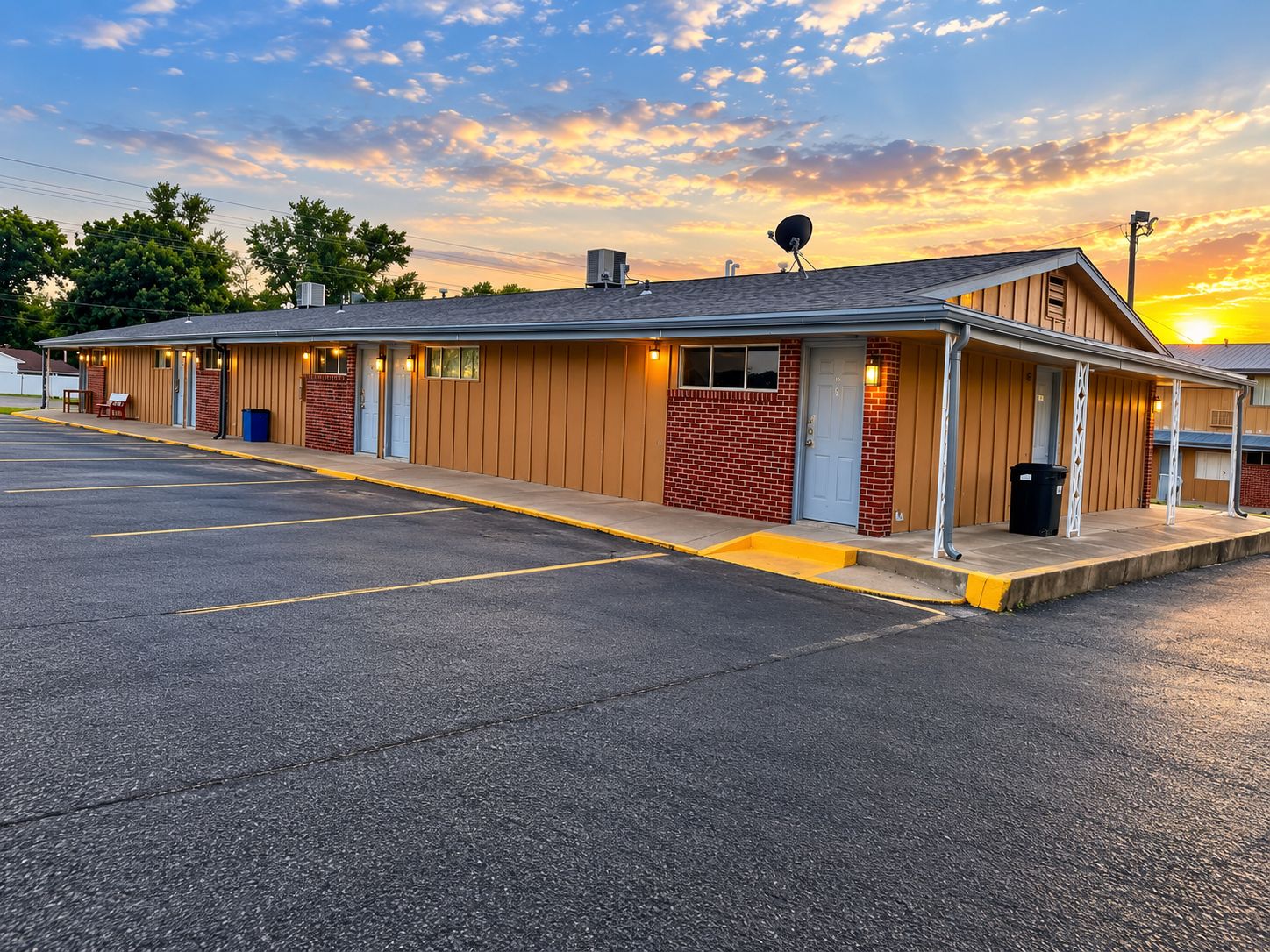 A motel with a row of rooms, a parking lot, and a sunset in the background.