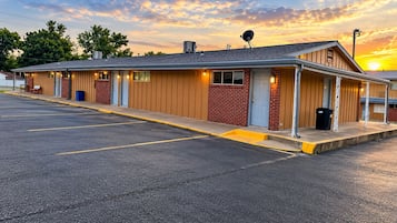A motel with a row of rooms, a parking lot, and a sunset in the background.