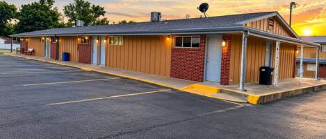A motel with a row of rooms, a parking lot, and a sunset in the background.