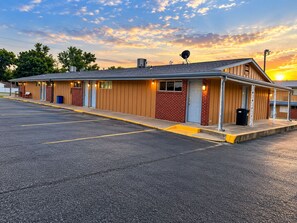 A motel with a row of rooms, a parking lot, and a sunset in the background. - Budget Lodge Inn Abilene KS (Abilene)