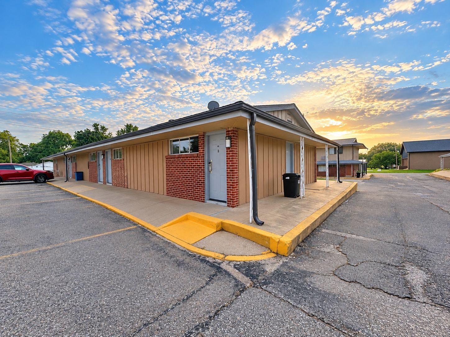 A single-story motel with a brick facade, a covered parking area, and a clear sky.