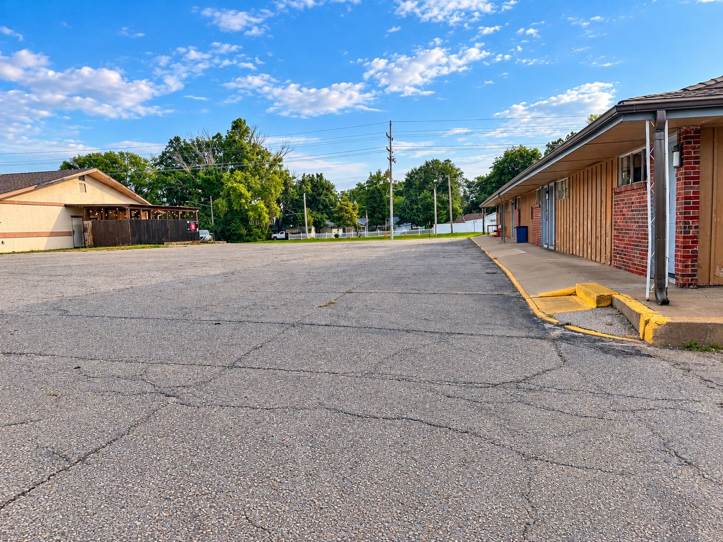 A parking lot with a building on the right and a fenced area on the left.