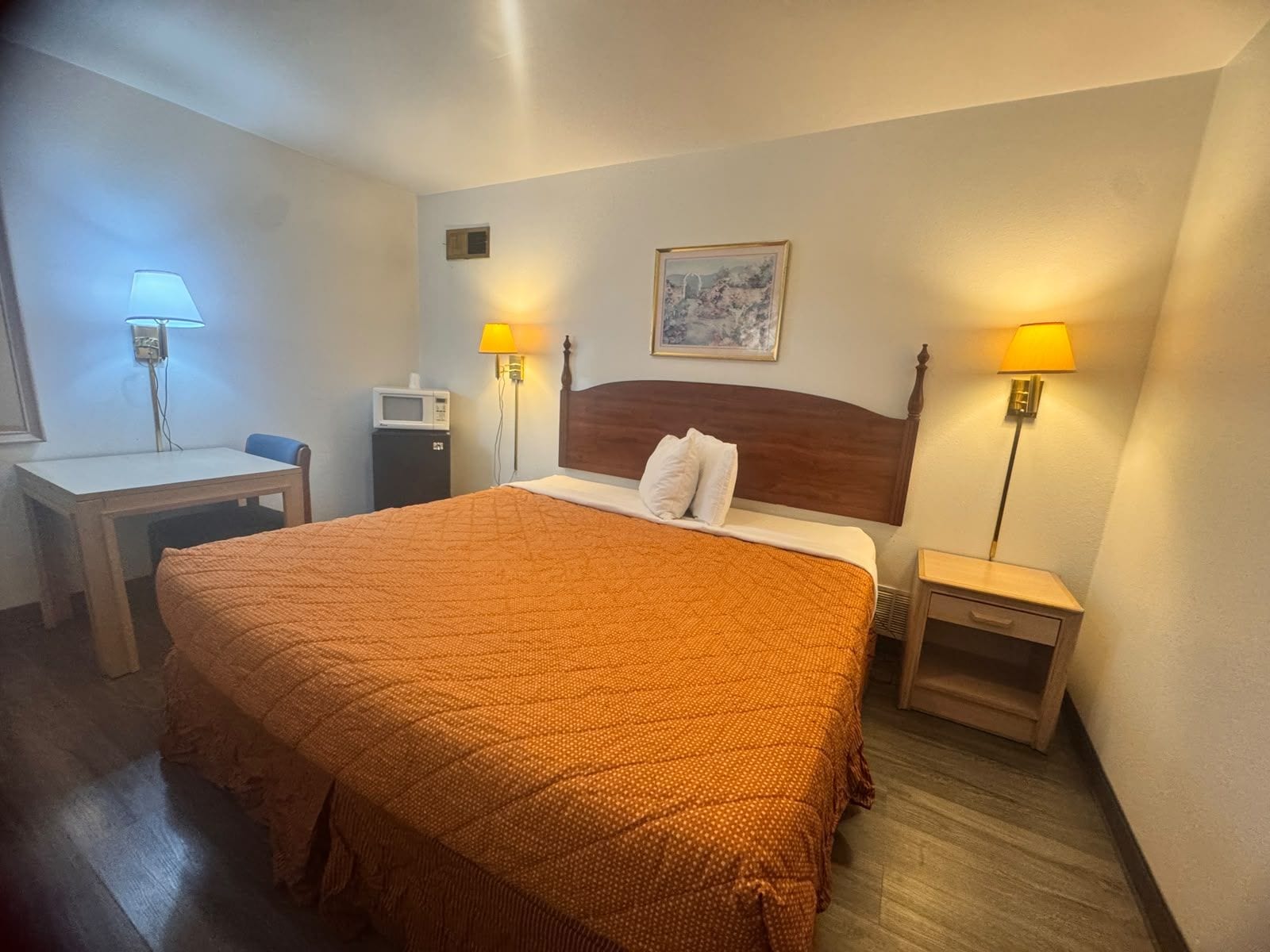 Una camera d'hotel con un letto, comodini, lampade, una TV a parete e un quadro.