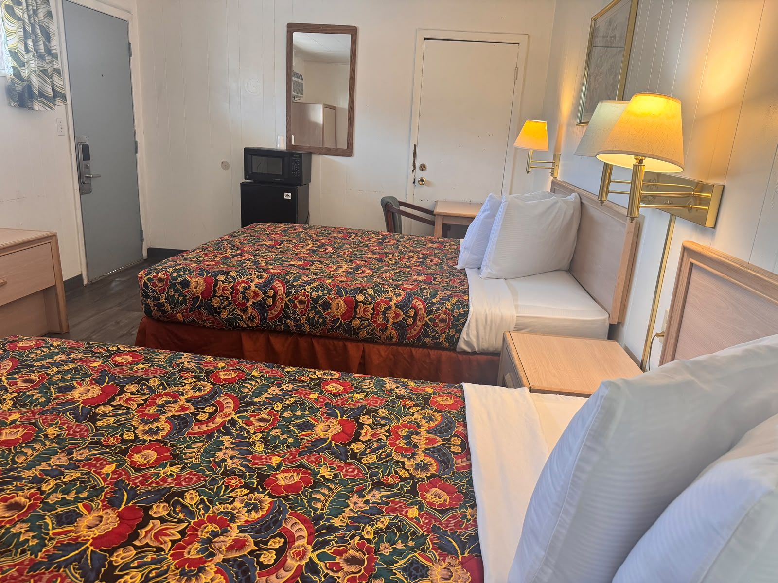 Une chambre d’hôtel avec deux lits, un bureau, une chaise, une lampe et un miroir.