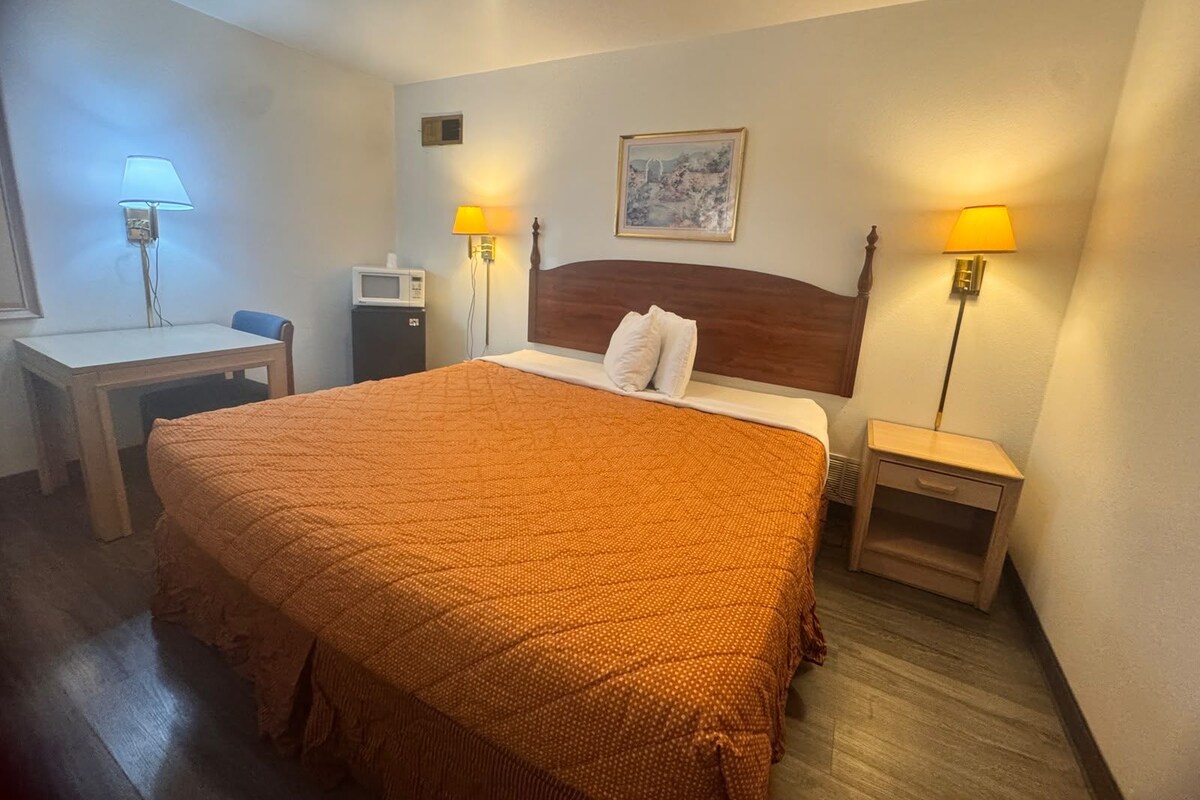 A hotel room with a bed, bedside tables, lamps, a wall-mounted TV, and a painting.