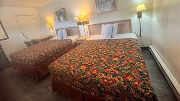 Una camera d'albergo con due letti, ognuno con una coperta a motivi floreali, una testiera in legno e lampade ai comodini.