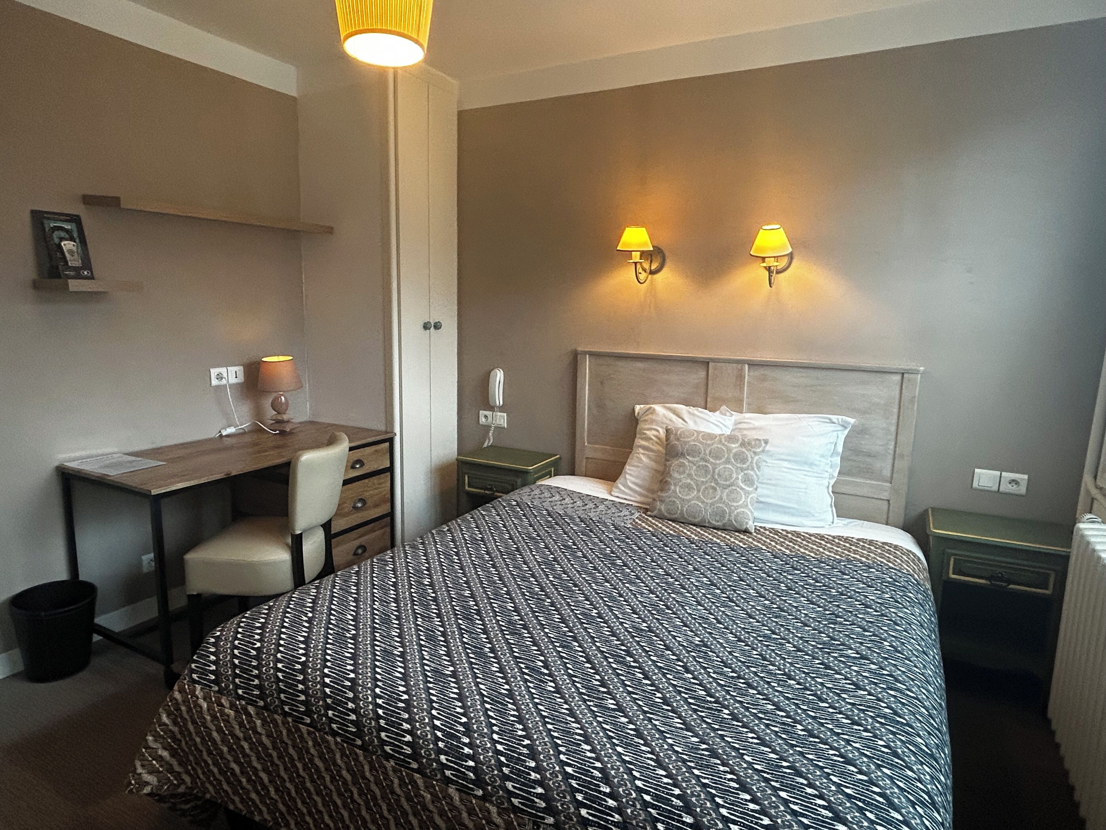 Una habitación de hotel con cama, escritorio, silla, dos lámparas de noche y teléfono.