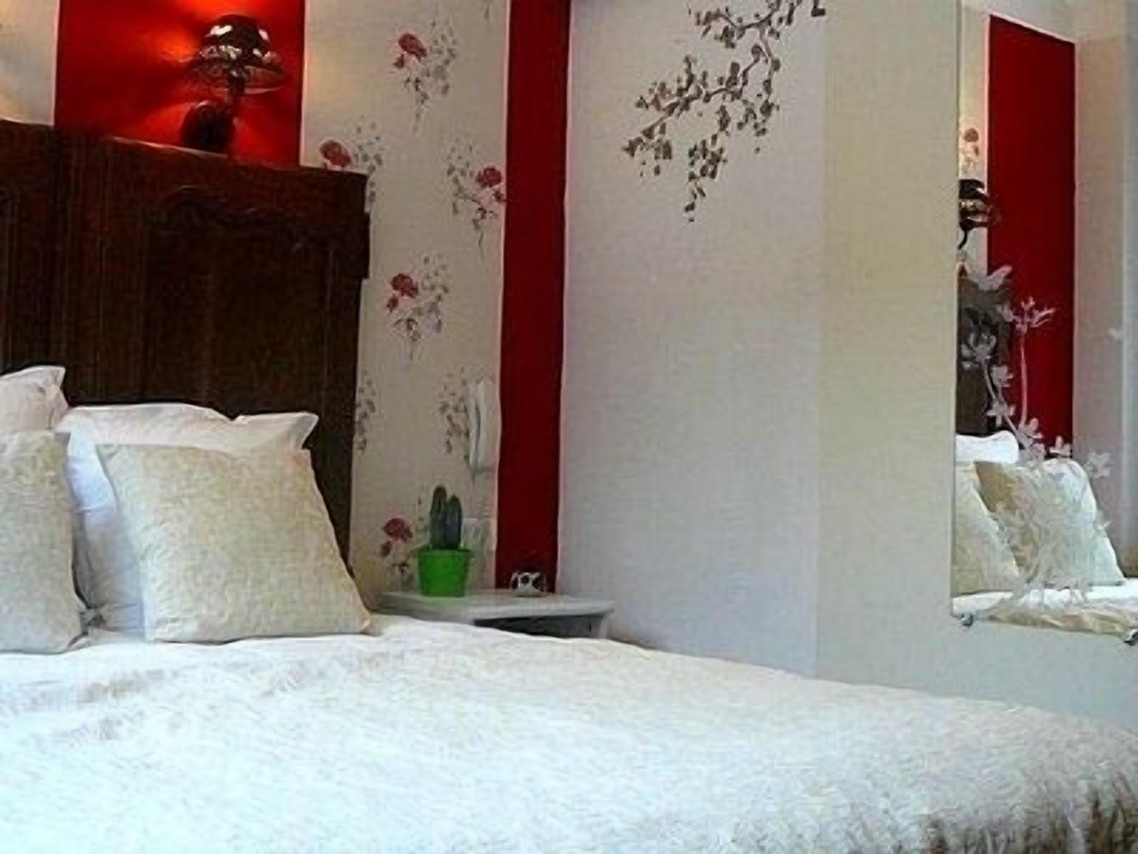 A bedroom with a bed, pillows, a nightstand, a mirror, and floral wall decorations.
