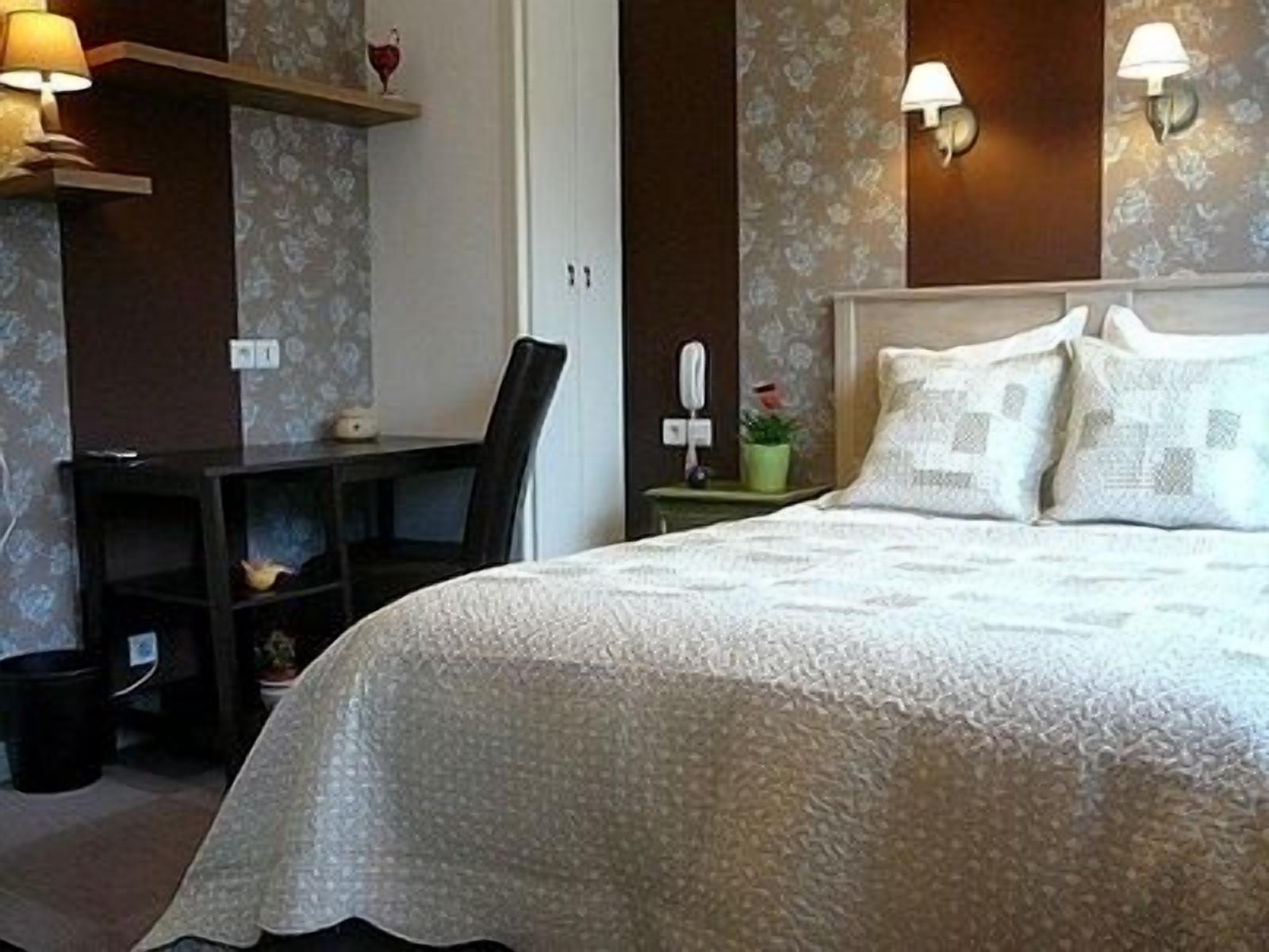A neatly arranged bedroom with a bed, bedside table, lamp, and a small desk with a chair.